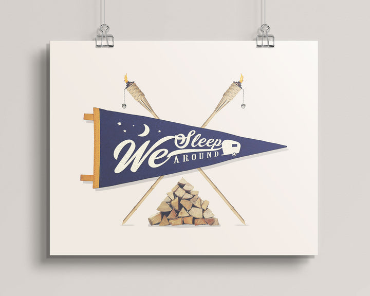 hanging wall artwork with a blue pennant, crossed sticks, and woodpile on a light background titled We Sleep Around