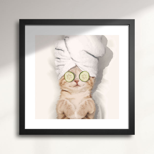 Framed artwork of a cat with a towel on its head and cucumbers on its eyes titled Spa Kitty
