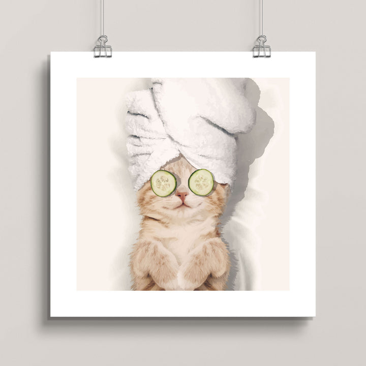 Hanging artwork of a cat with a towel on its head and cucumbers on its eyes titled Spa Kitty